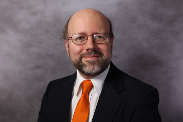 Peter J. Wasilko wearing a dark suit and orange tie.